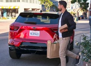 A person holding a shopping bag walking behind their red 2024 Chevrolet Blazer near Anderson, Indiana
