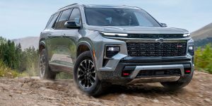 A gray 2025 Chevrolet Traverse SUV driving on a rugged mountain trail, highlighting its bold design, all-terrain capability, and modern performance.