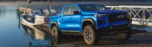 Blue 2026 Chevrolet Colorado towing a boat at a lakeside ramp.