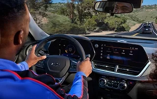 A driver's view of a Chevrolet instrument cluster and touchscreen on a winding highway