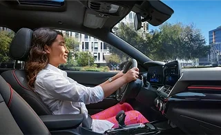 A smiling driver with both hands on the wheel of a Chevrolet on a sunny city street