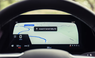 A Chevrolet digital instrument cluster showing a map with turn-by-turn directions, seen through the steering wheel