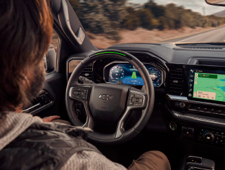 A driver behind the wheel of a Chevrolet with the steering-wheel light bar lit green and a map on the touchscreen