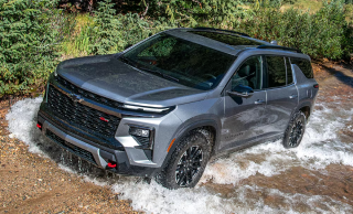 A gray Chevrolet Equinox splashing through a shallow stream on a dirt trail
