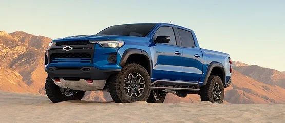 A blue Chevrolet Colorado parked on desert sand with mountains behind it