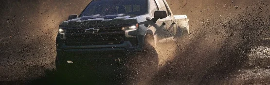 A Chevrolet Silverado 1500 Trail Boss throwing mud as it powers through a rutted track