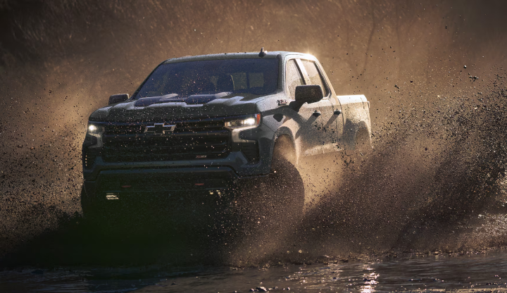 A Chevrolet Silverado 1500 Trail Boss driving through deep water and throwing spray