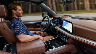 A driver at the wheel of a Chevrolet with a brown leather interior and navigation on the display