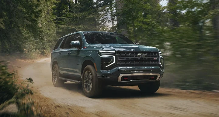 A dark Chevrolet Tahoe driving down a dirt road through a forest
