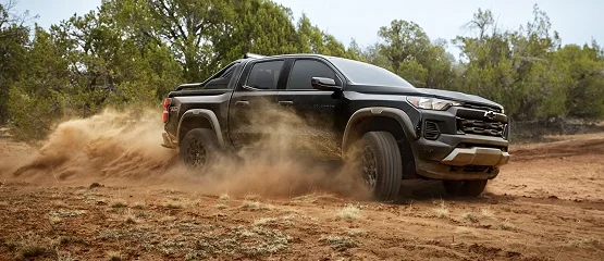 A black Chevrolet Colorado kicking up dust on a dirt trail