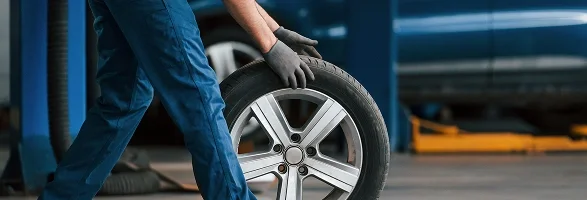 A technician in gloves rolling a tire and alloy wheel across a service bay