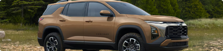 A bronze 2027 Chevrolet Equinox parked on grass in front of pine trees