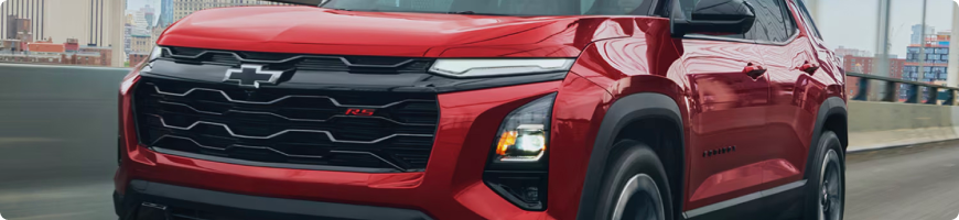 Grille and headlights of a red 2027 Chevrolet Equinox RS driving through a city